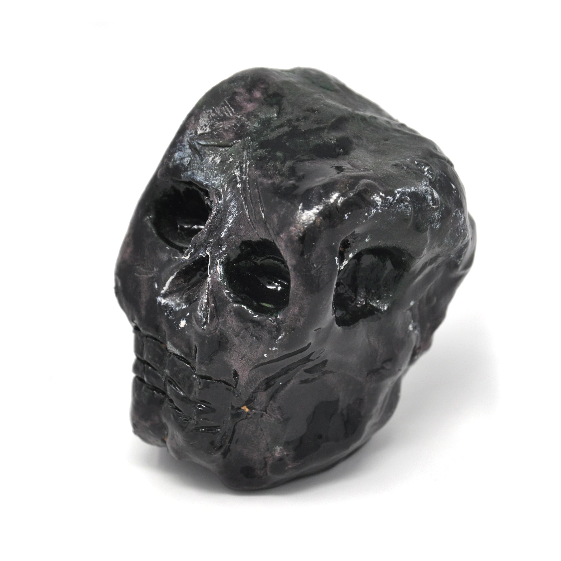 a ceramic sculpture of a smiling skull, painted all black, facing toward the left in this image.