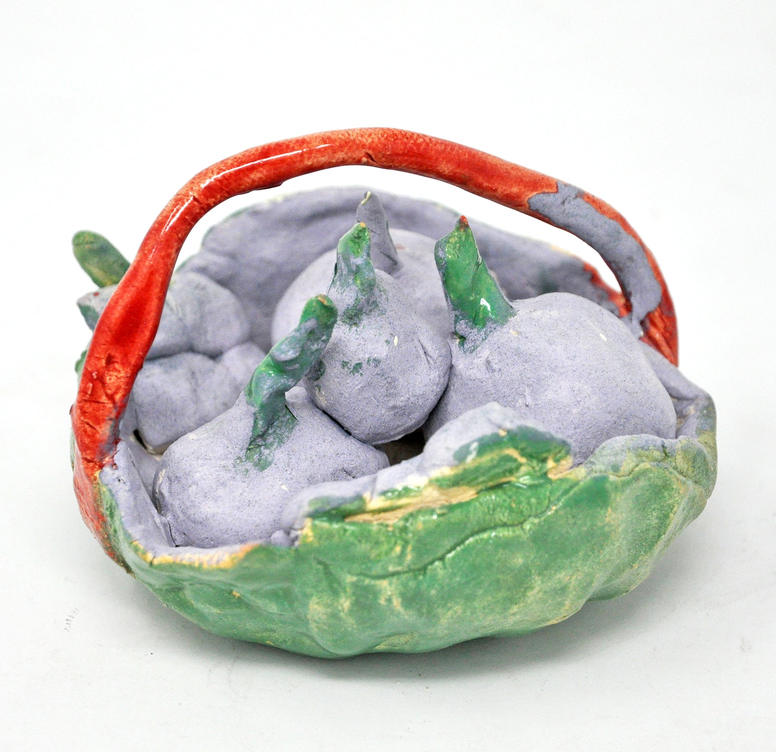 a miniature ceramic sculpture titled Cherry Basket. The form is a shallow green bowl with a red handle arching over the top. in the bowl are grey orbs with green stems.