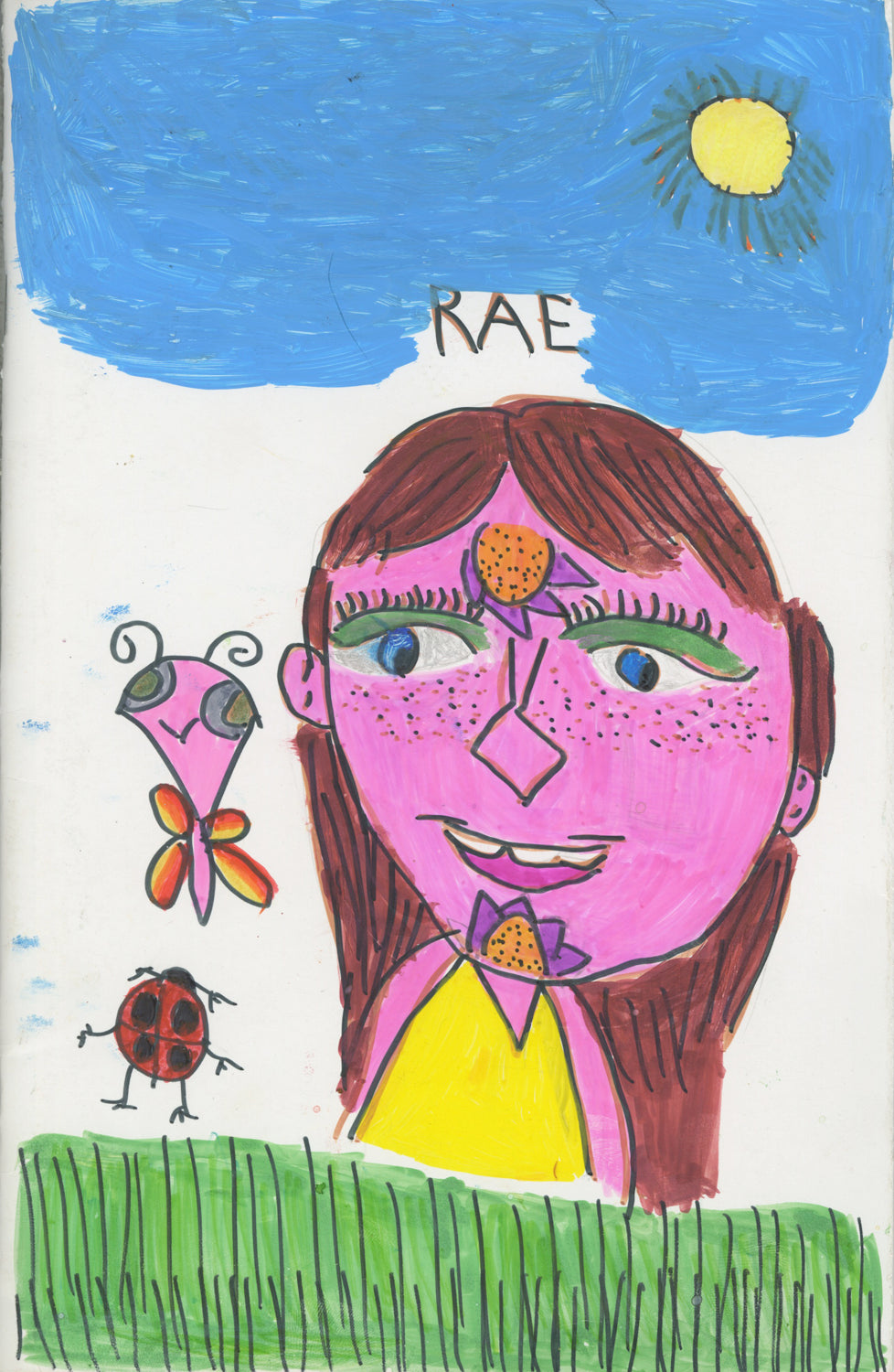 The  cover of a handmade artist book. The cover has a drawing of a large smiling figure, depicted from the shoulder up, in a green field. The figure has pink skin, long brown hair, and a yellow shirt. There are flowers drawn on the forehead and chin of the figure's face. Next to the figure is a ladybug and a butterfly. There is a blue stripe of sky across the top half of the paper with a small yellow sun. the artist's name "RAE" is written in the sky. 