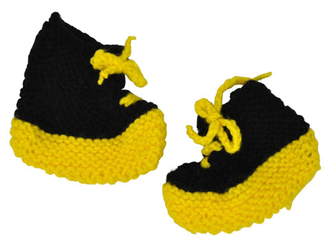 A pair of hand knitted baby booties made of black and yellow yarn. Each black shoe has hand-knit yellow laces tied in a bow, and yellow soles. 