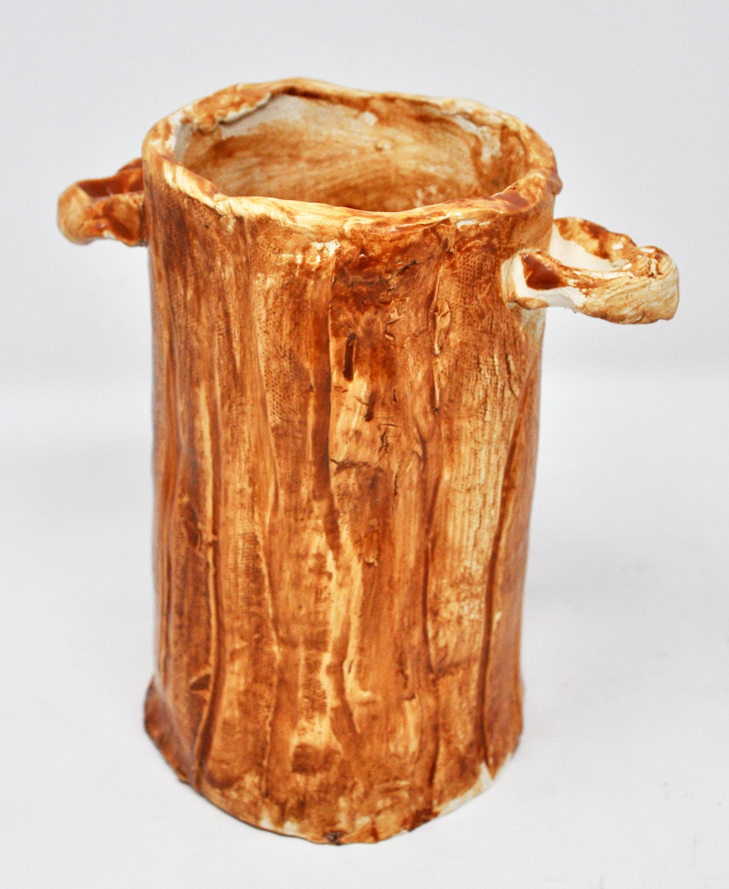 a tall glazed ceramic vessel painted in washes of brown glaze. The vessel has two little loop handles attached near its opening. The texture and shape are reminiscent of a tree trunk.