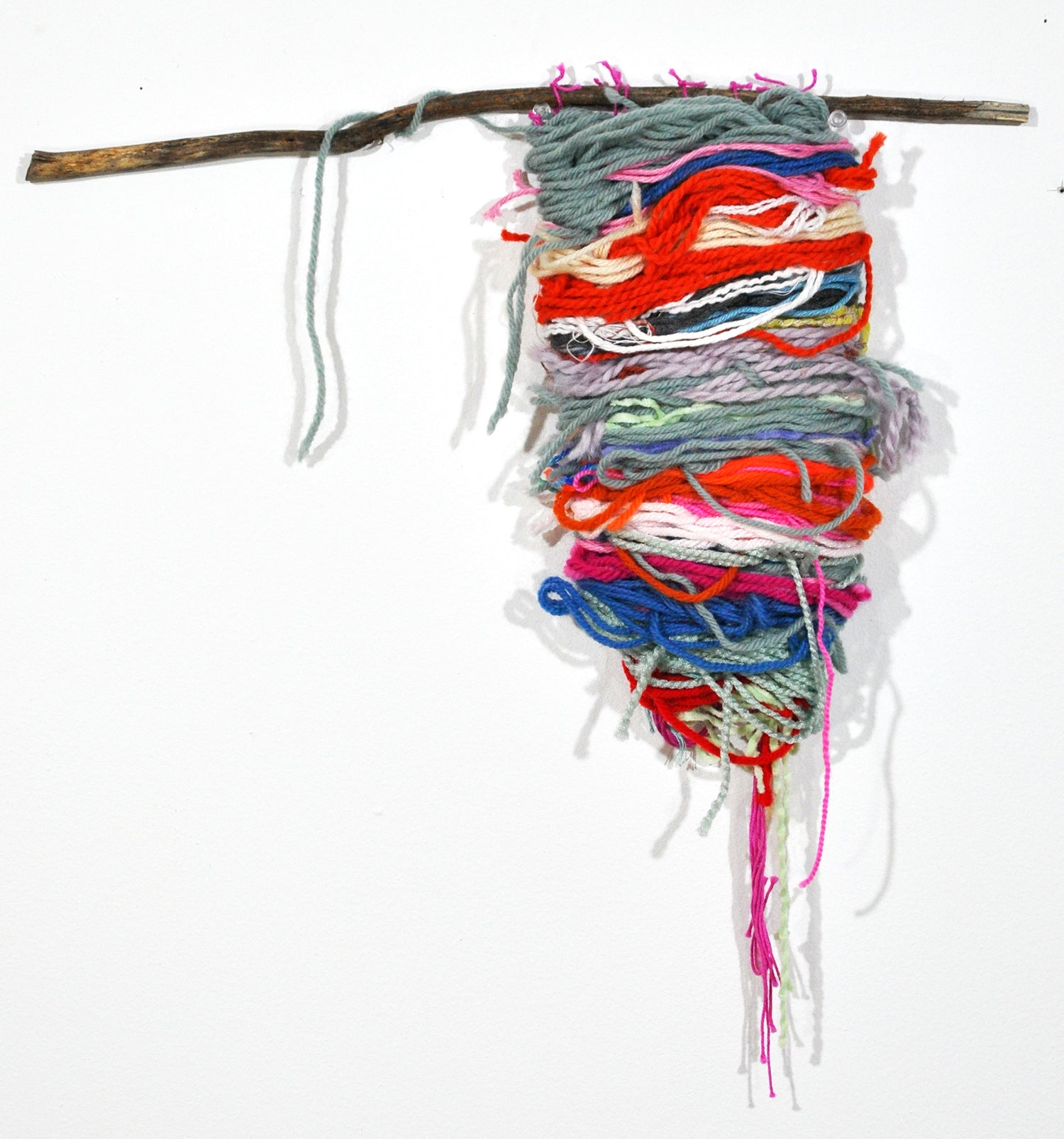 a small handwoven cloth hanging from a wooden branch. the cloth is horizontal stripes of grey, red, pink, and blue yarn.