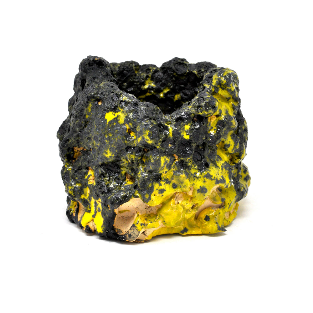 a yellow and black ceramic pot vessel with a lumpy texture and both shiny and matte thick glazed coating. The black glaze has a rough and pocked texture like lava rock. The yellow areas peak out from beneath the black glaze, and are a contrasting smooth and glossy texture, like glass.