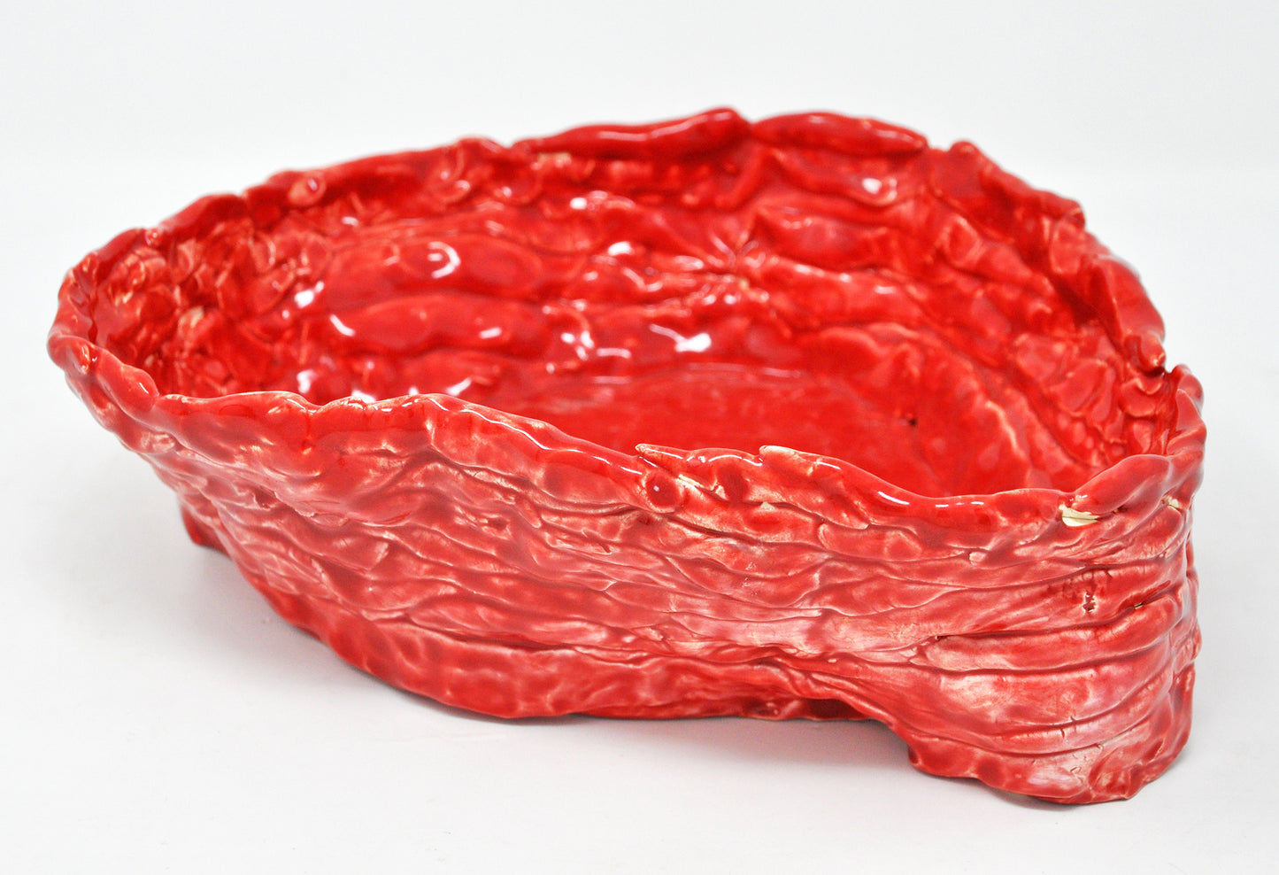 A glazed ceramic coil pot photographed on a white backdrop. The vessel oblong with a wide opening. The entire sculpture is glazed a shiny bright red.