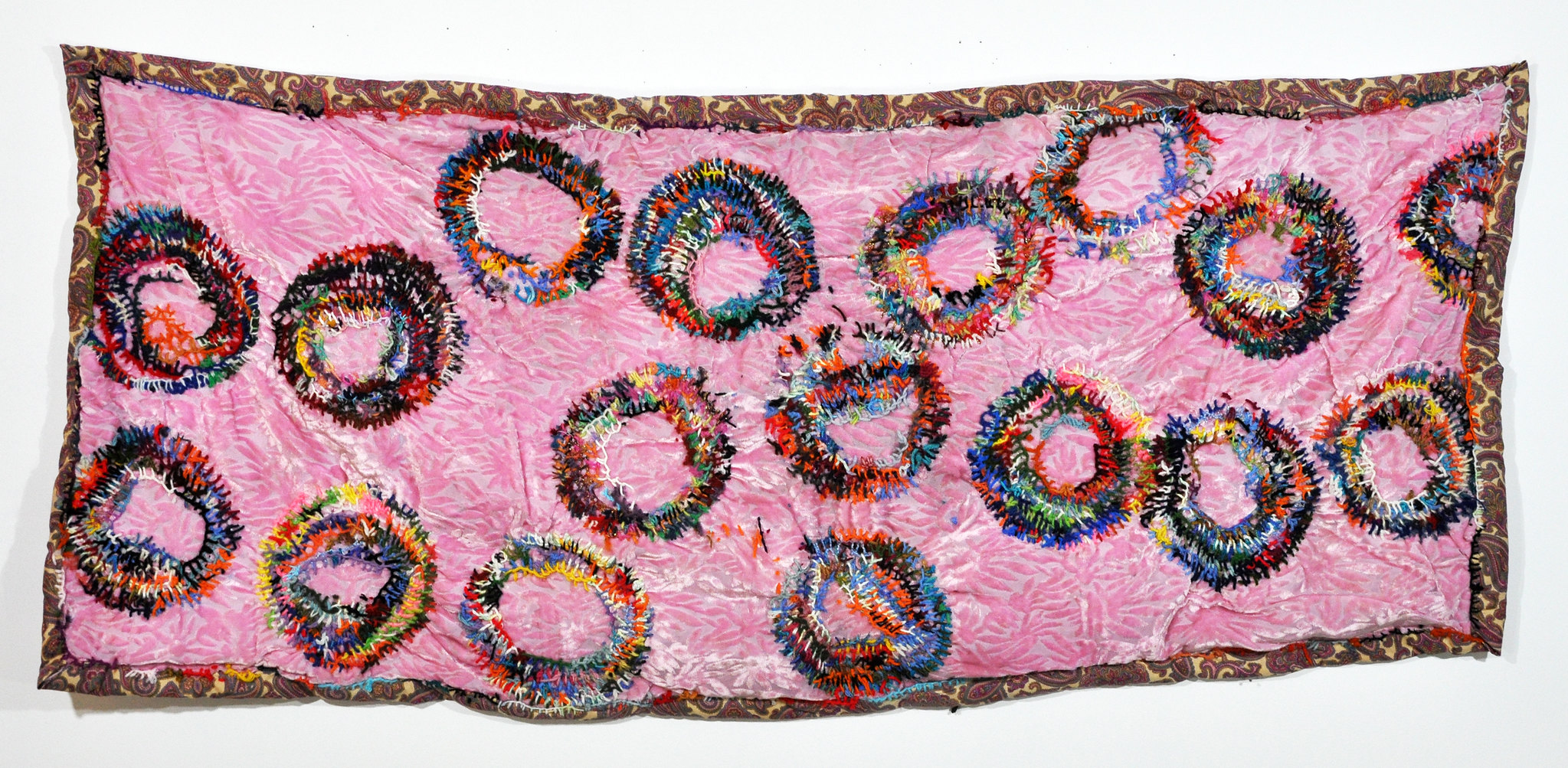 Large pink quilt with circles of sewn very colorful yarn.