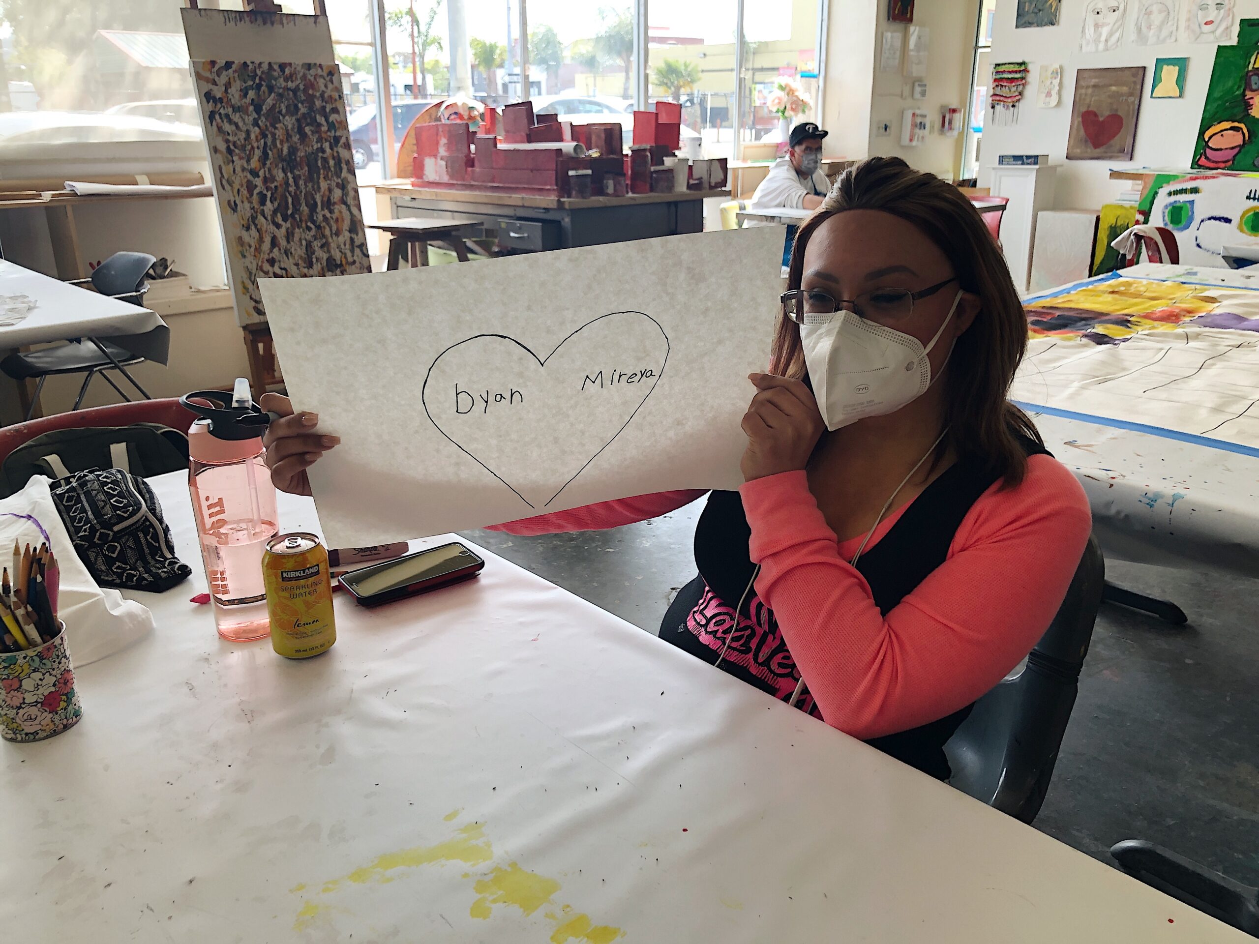 Artist Mireya holds up a picture of a large heart in the NIAD studio
