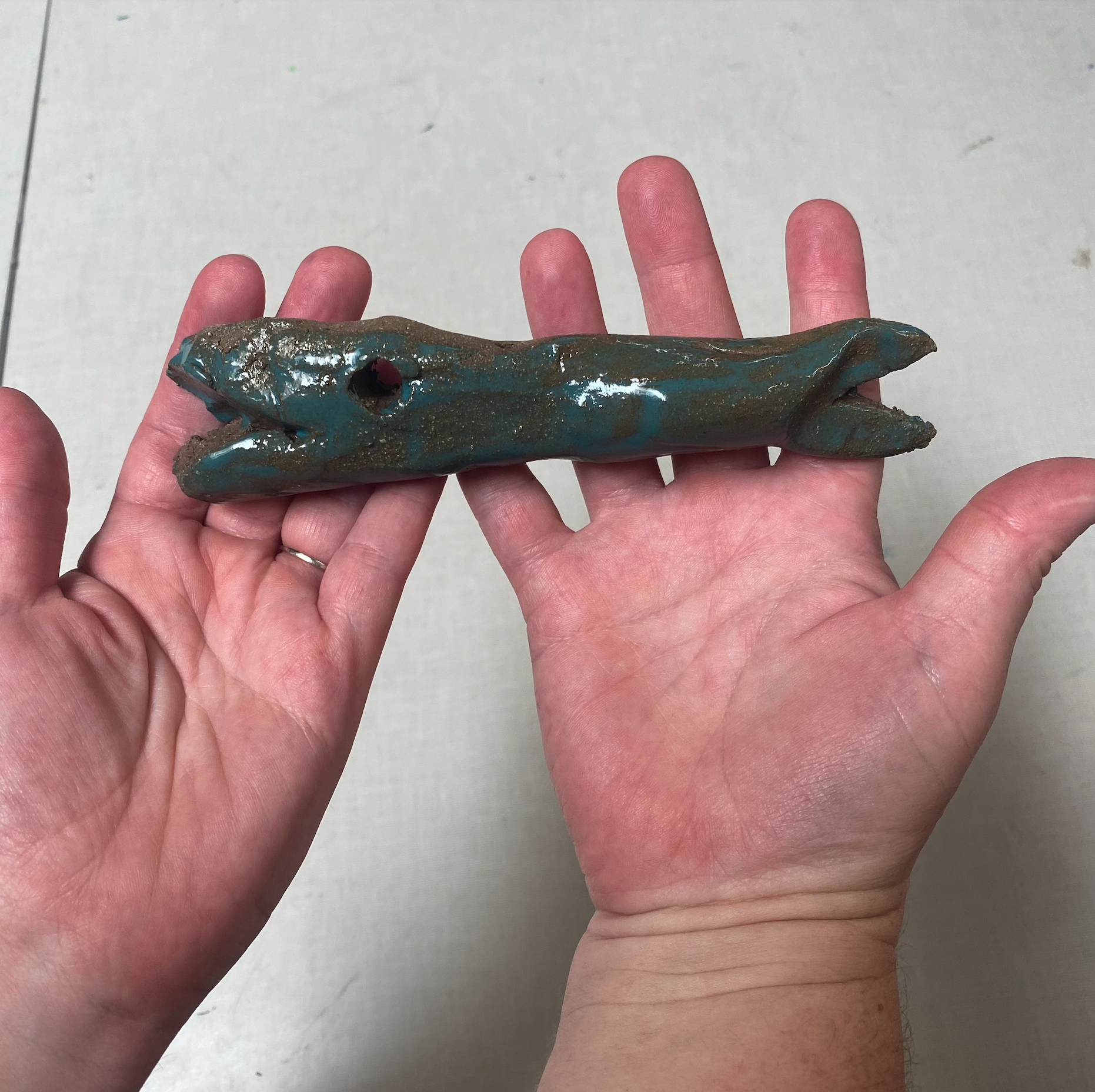A person holds a small green fish-shaped ceramic sculpture.