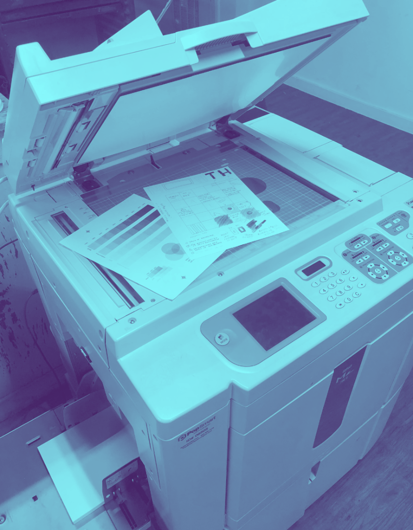 a blue-tinted photograph of riso prints on a risograph machine.