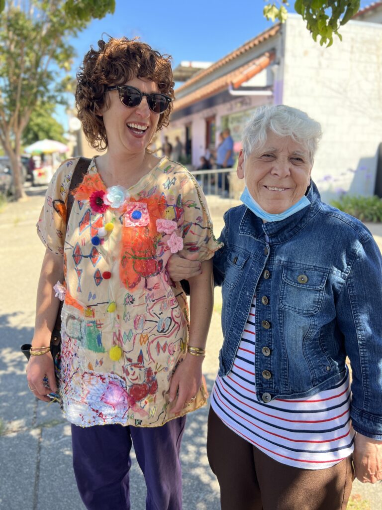 Volunteer at NIAD. Cheery, bright outdoor photo portrays NIAD artist Karen May standing next to a friend. Both are smiling and laughing at the camera.